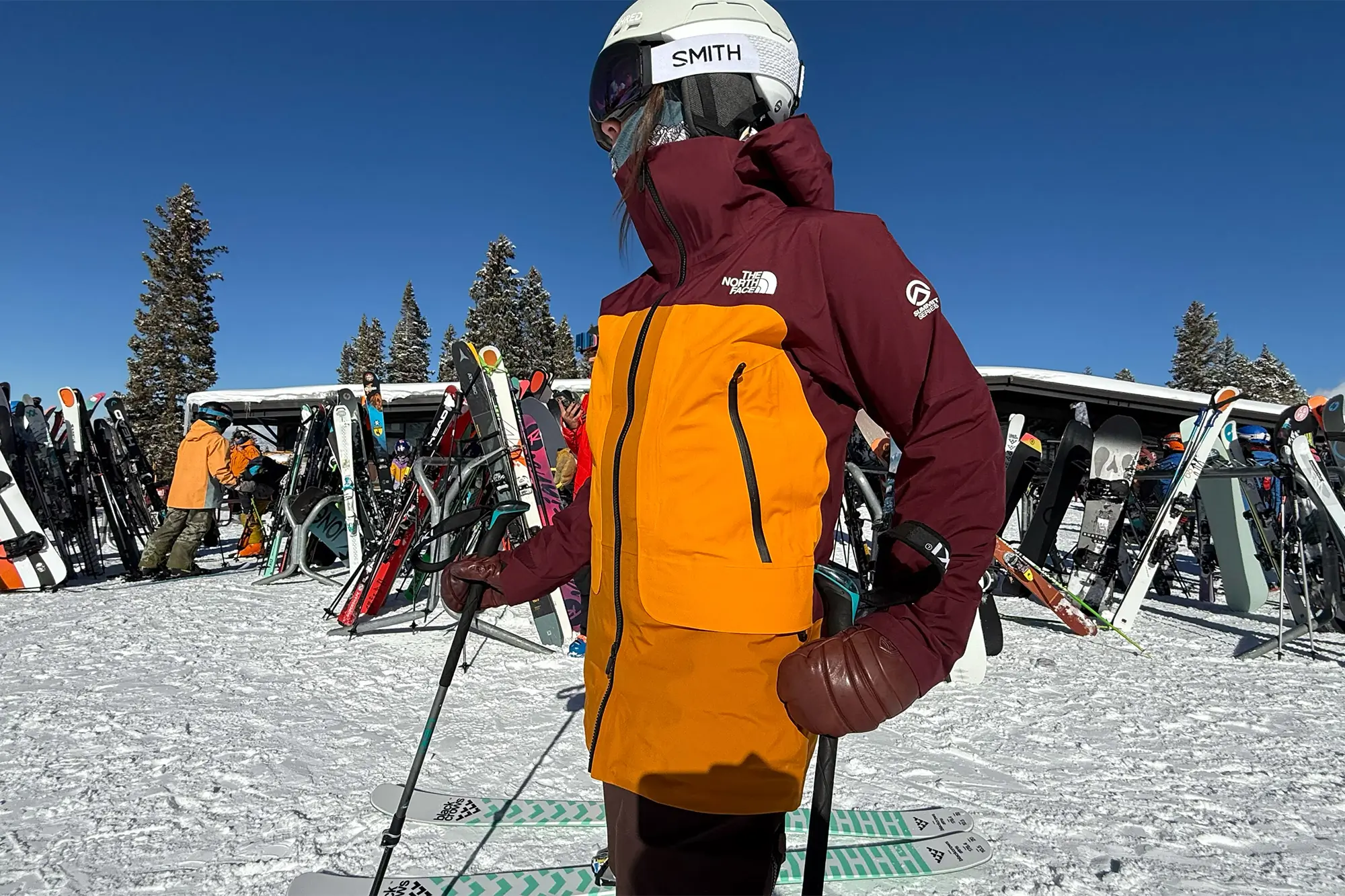 A skier wearing The North Face Summit Series Verbier Gore-Tex Jacket in vibrant maroon and orange, paired with a white helmet and reflective goggles.