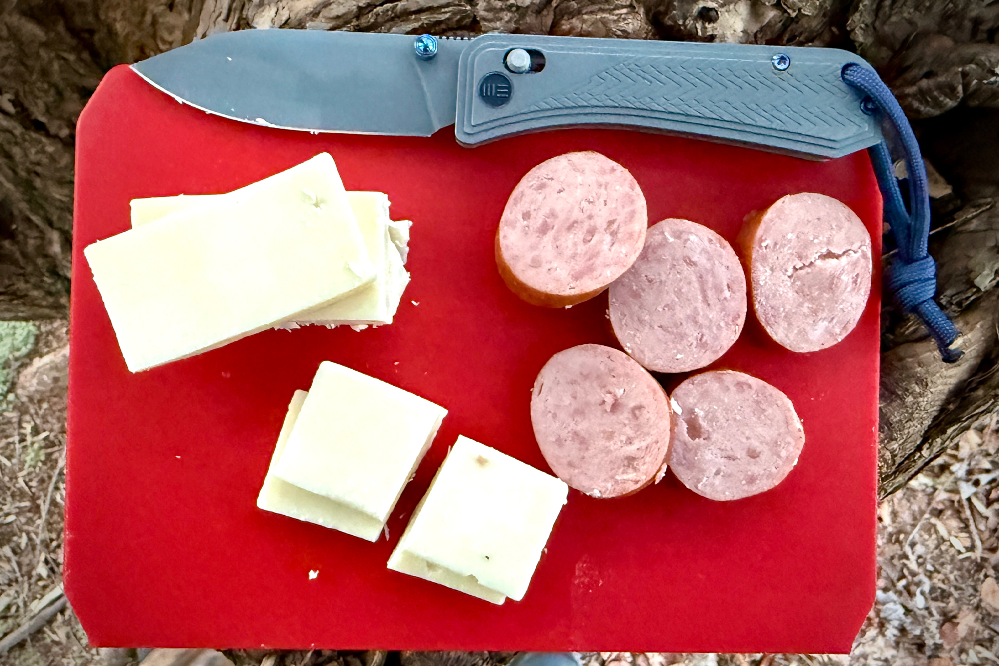 The WE Knife Bougie resting on a red cutting board with sliced sausage and cheese, showcasing its versatility for food prep