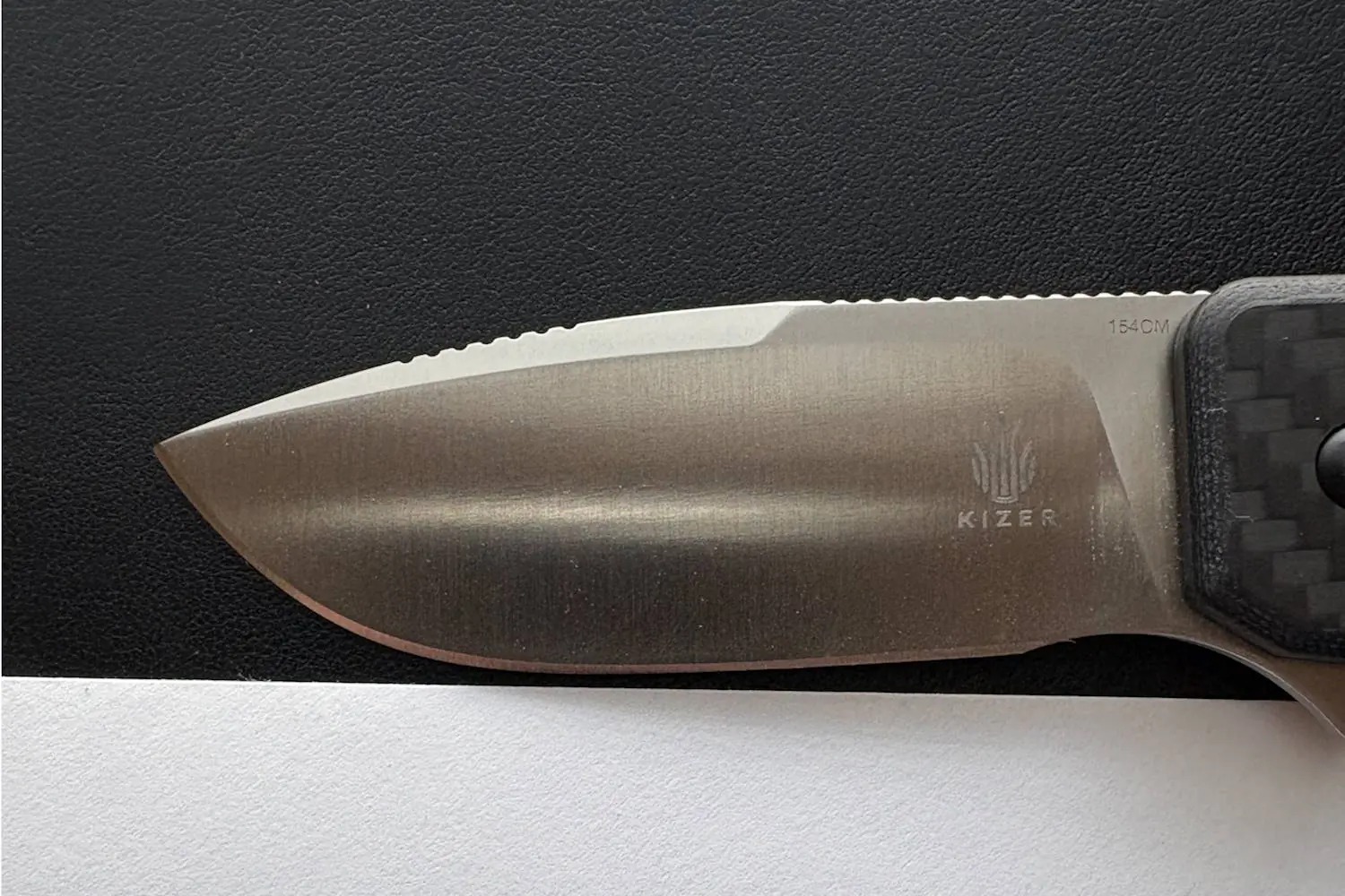 Close-up of a Kizer knife blade with a carbon fiber handle