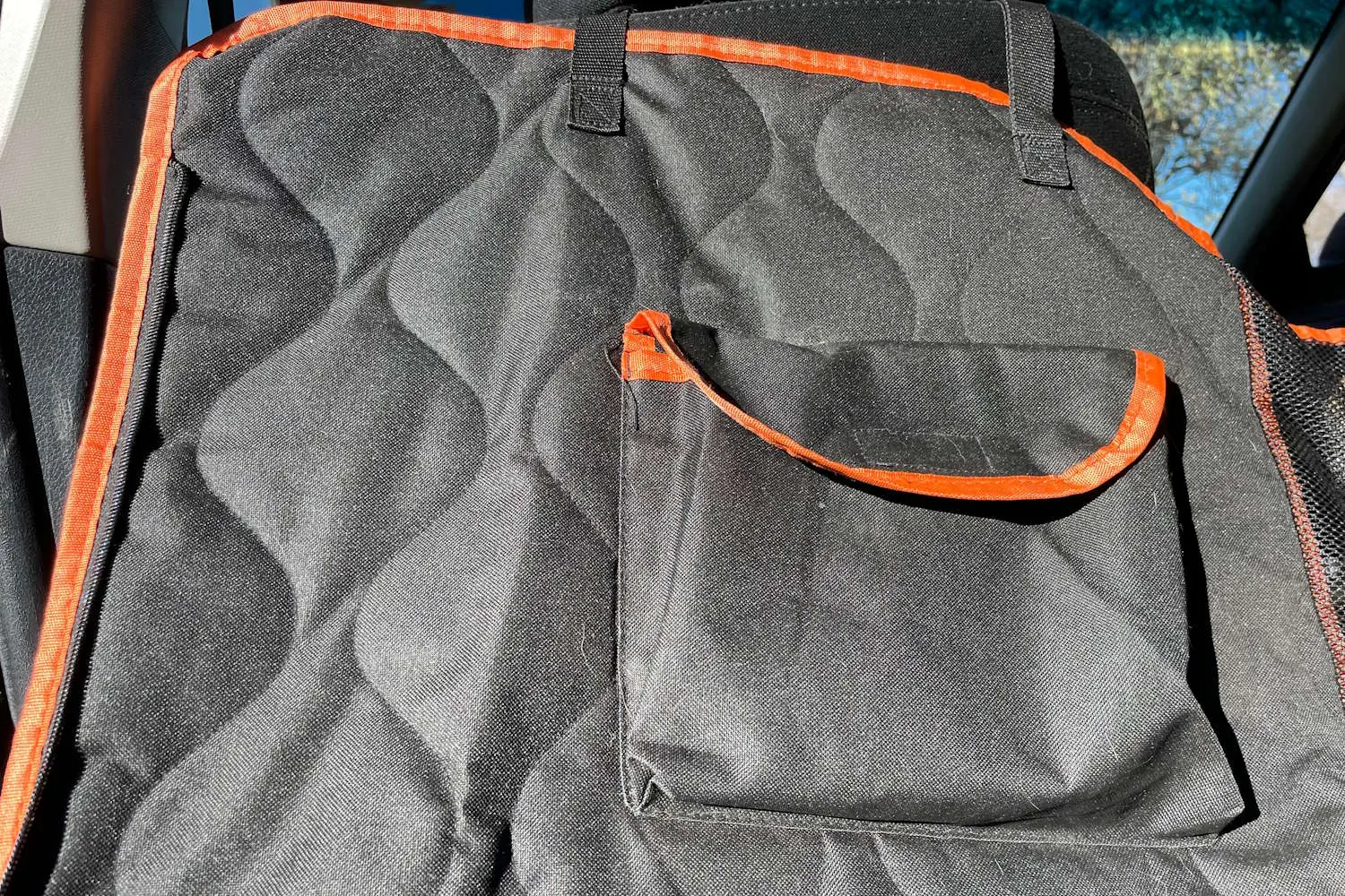 Close-up of a black quilted waterproof car seat cover featuring a storage pocket