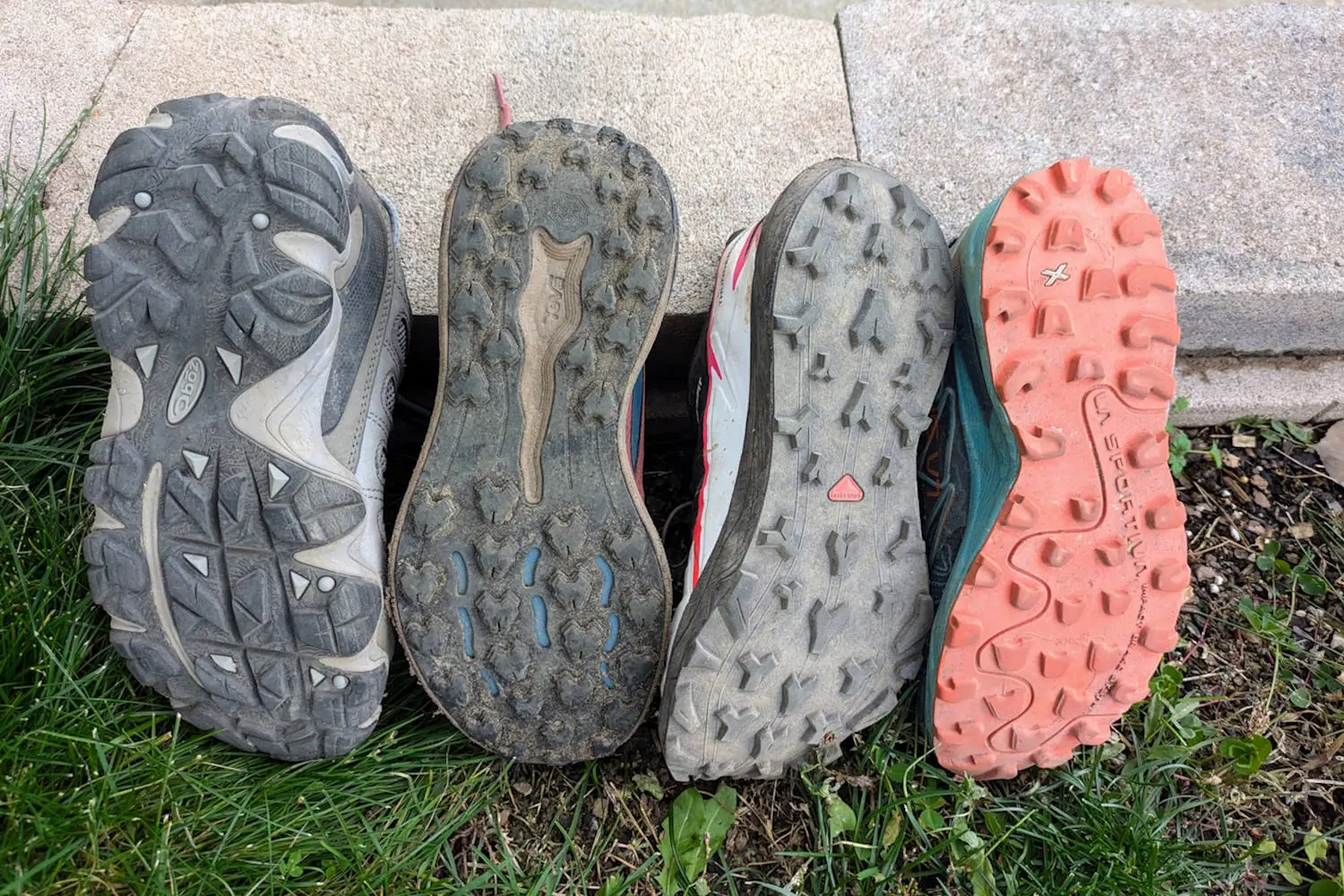 Four trail running shoe soles displayed side by side