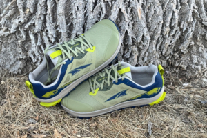 Altra Lone Peak 9 trail runners with a green and blue colorway resting against a tree trunk