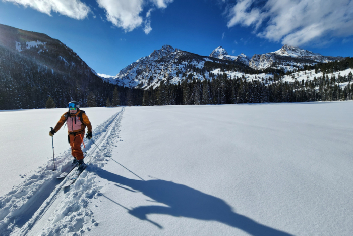 A skier crossing an open snowfield with towering mountains in the background