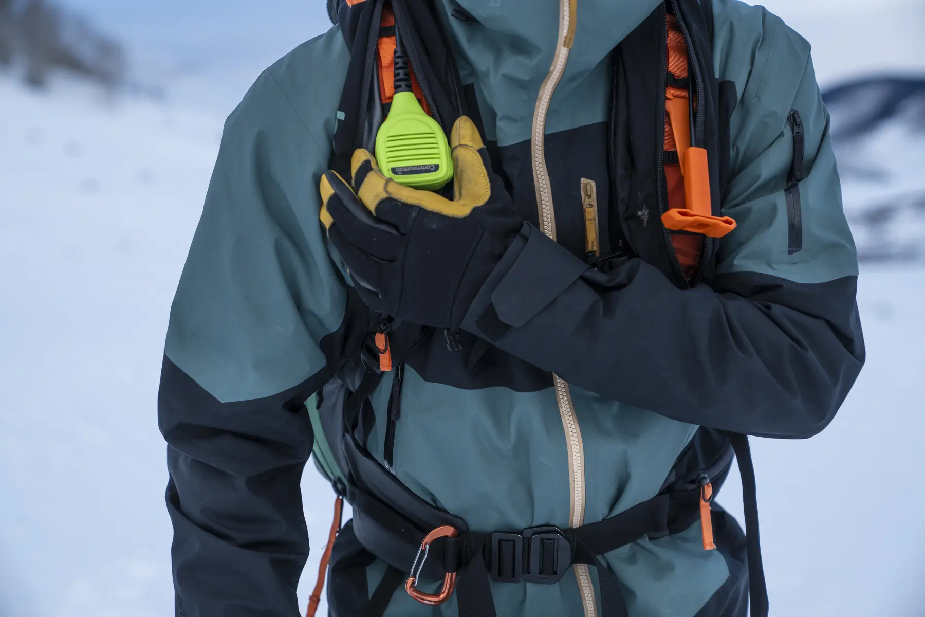 Hand holding a radio clipped to the BCA Float E2-35 Avalanche Airbag strap