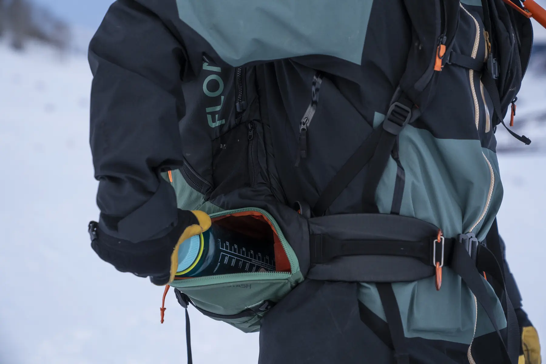 Gloved hand reaching into the hip pocket of the BCA Float E2-35 Avalanche Airbag for a water bottle