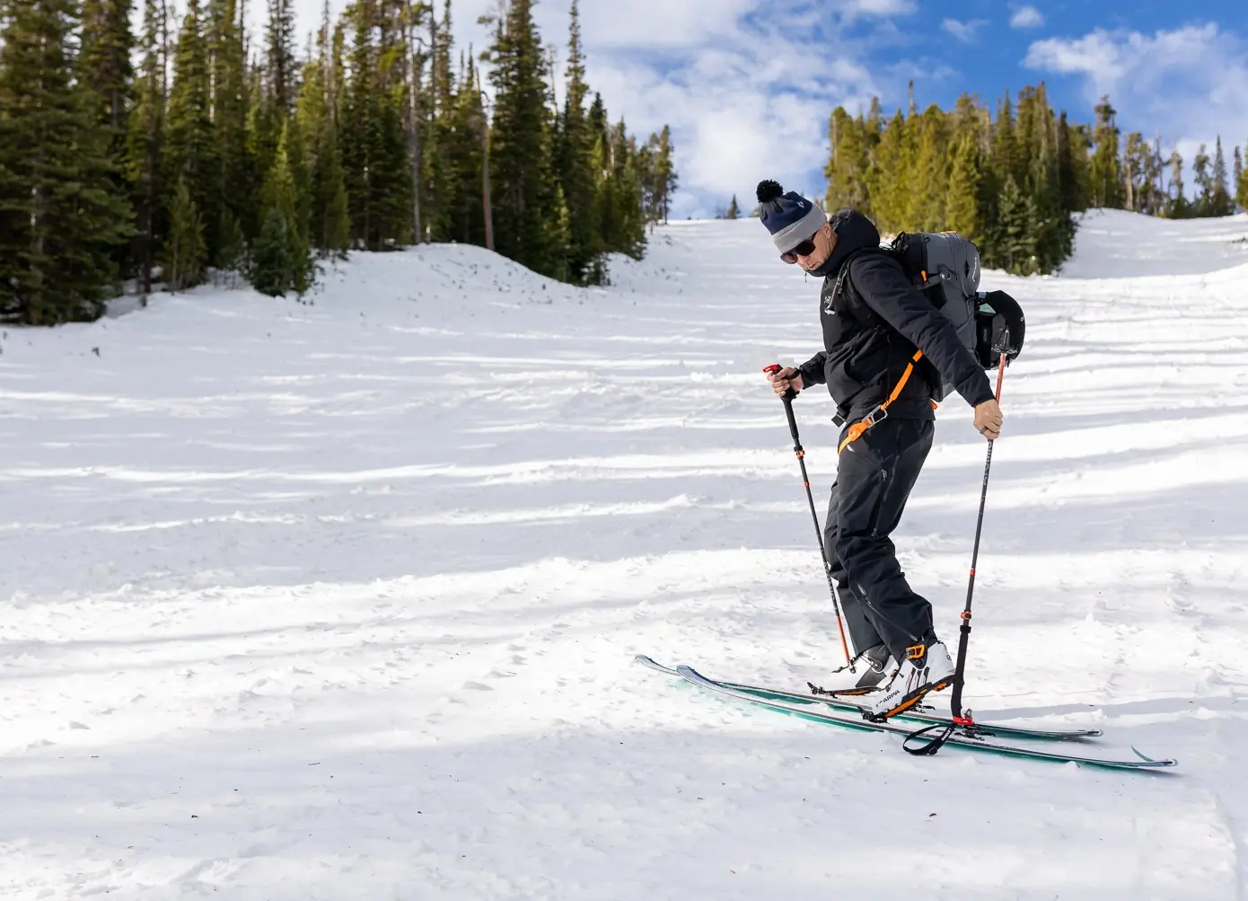 A skier ascends on Dynafit Seven Summits skis with poles, wearing a backpack on a snowy slope
