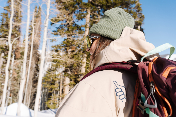 Close-up of a person wearing the Trew Gear Women’s Stella Jacket PRIMO-Plus with a backpack in a snowy forest