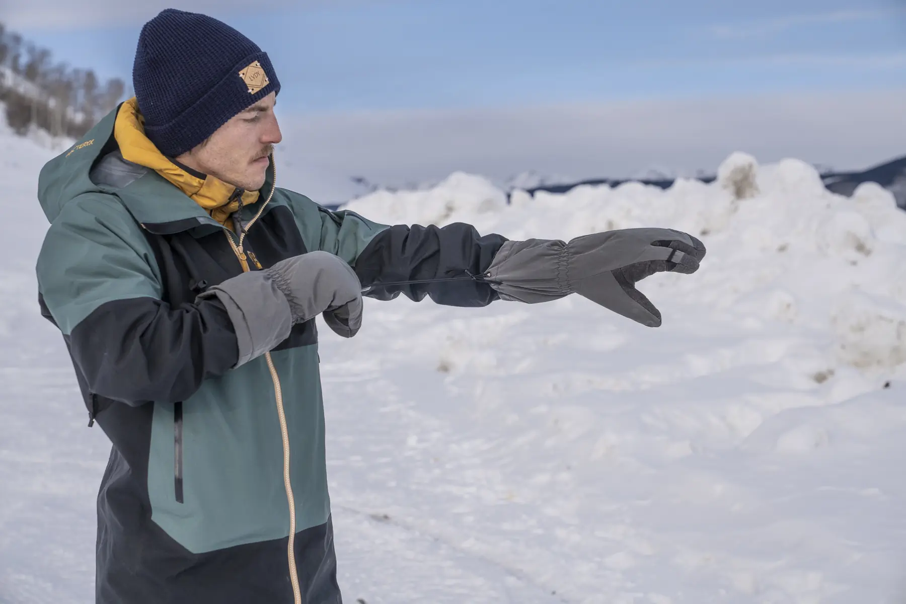 A man puts on a Kuiu Northstar Glomitt, showing its mitten and finger separation design