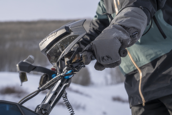 A close-up of a gloved hand adjusting the throttle on a snowmobile