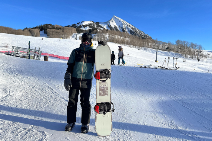 A snowboarder holding the Rome Stale Crewzer with the Crested Butte ski area in the background