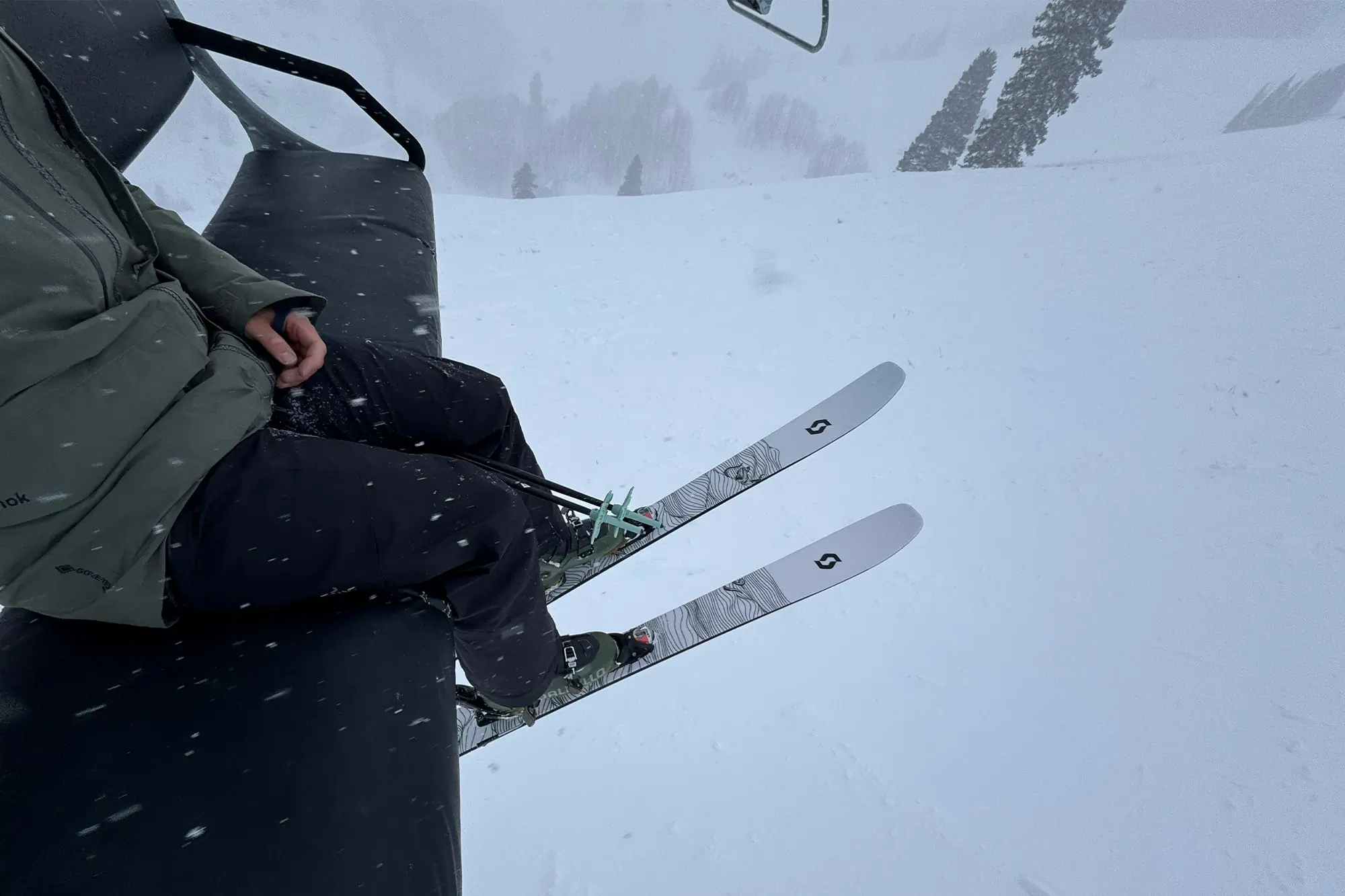 A rider on a lift with the Scott SEA 108 skis dangling over the slope