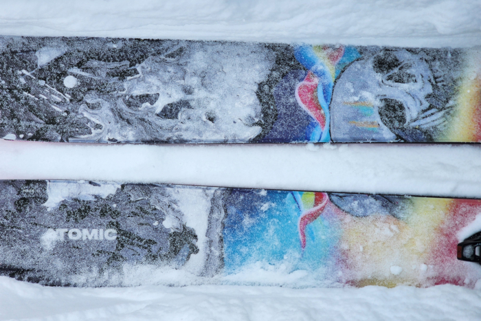 A close-up of the topsheets of Atomic Bent Chetler skis covered in snow