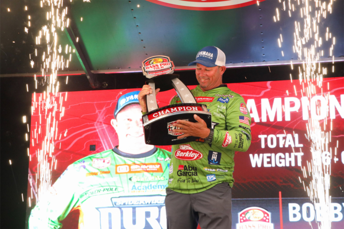 Bobby Lane celebrates his Bass Pro Tour win, holding a champion trophy as sparks fly on stage