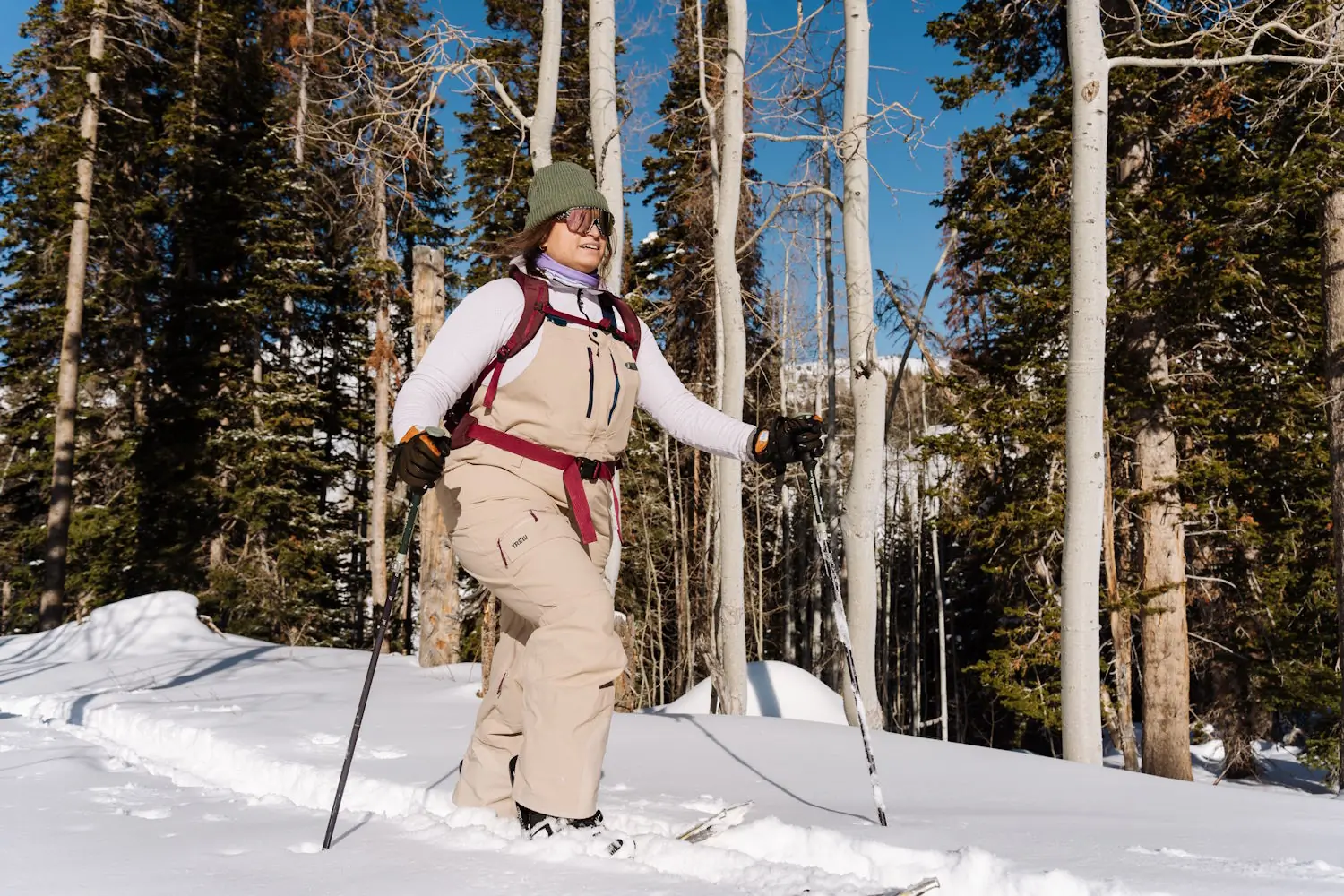 A woman wearing TREW Gear Chariot Plus Bibs is skiing through deep snow, using poles