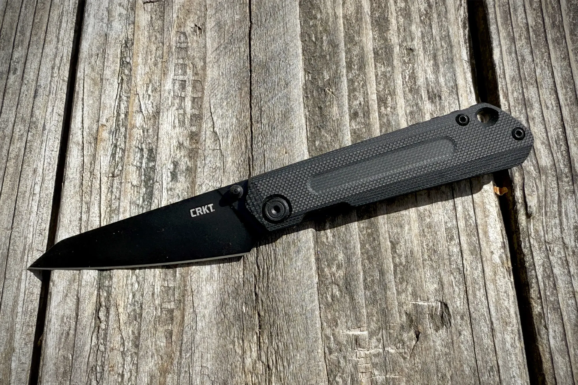 CRKT Straight with its blacked-out wharncliffe blade and G10 handle rests on a weathered wooden surface