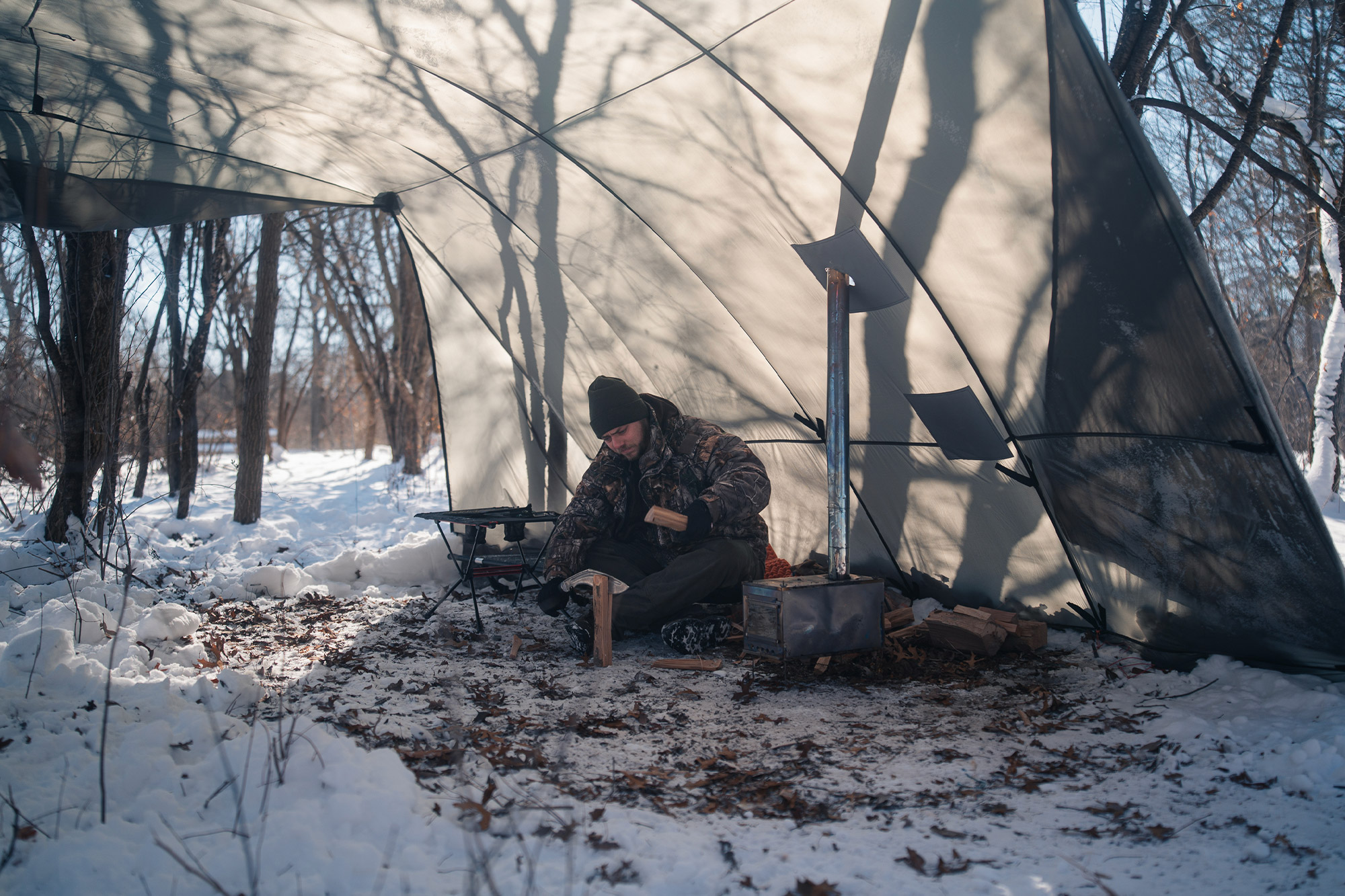 Camper splits wood inside the Warbonnet Tsunami, with a stove providing warmth