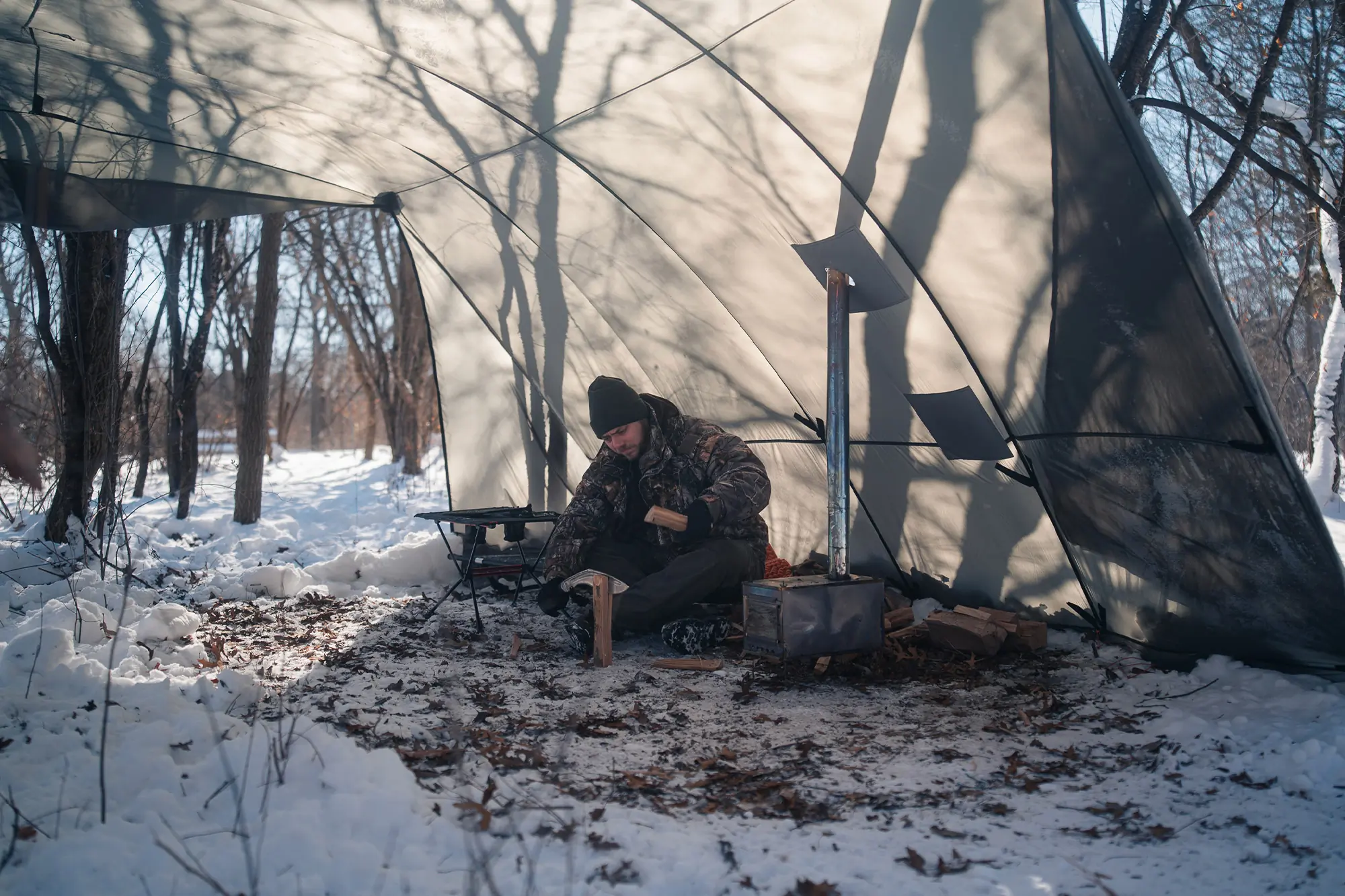 Camper splits wood inside the Warbonnet Tsunami, with a stove providing warmth
