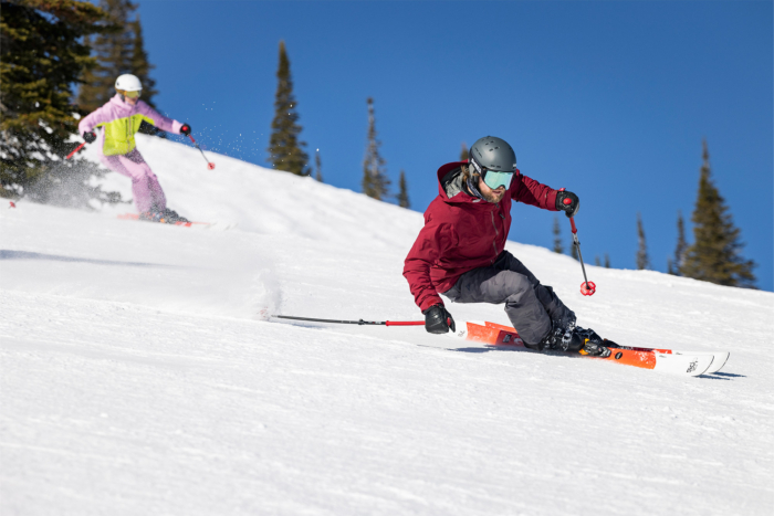 A skier in a red jacket carving a turn on the slopes, kicking up snow