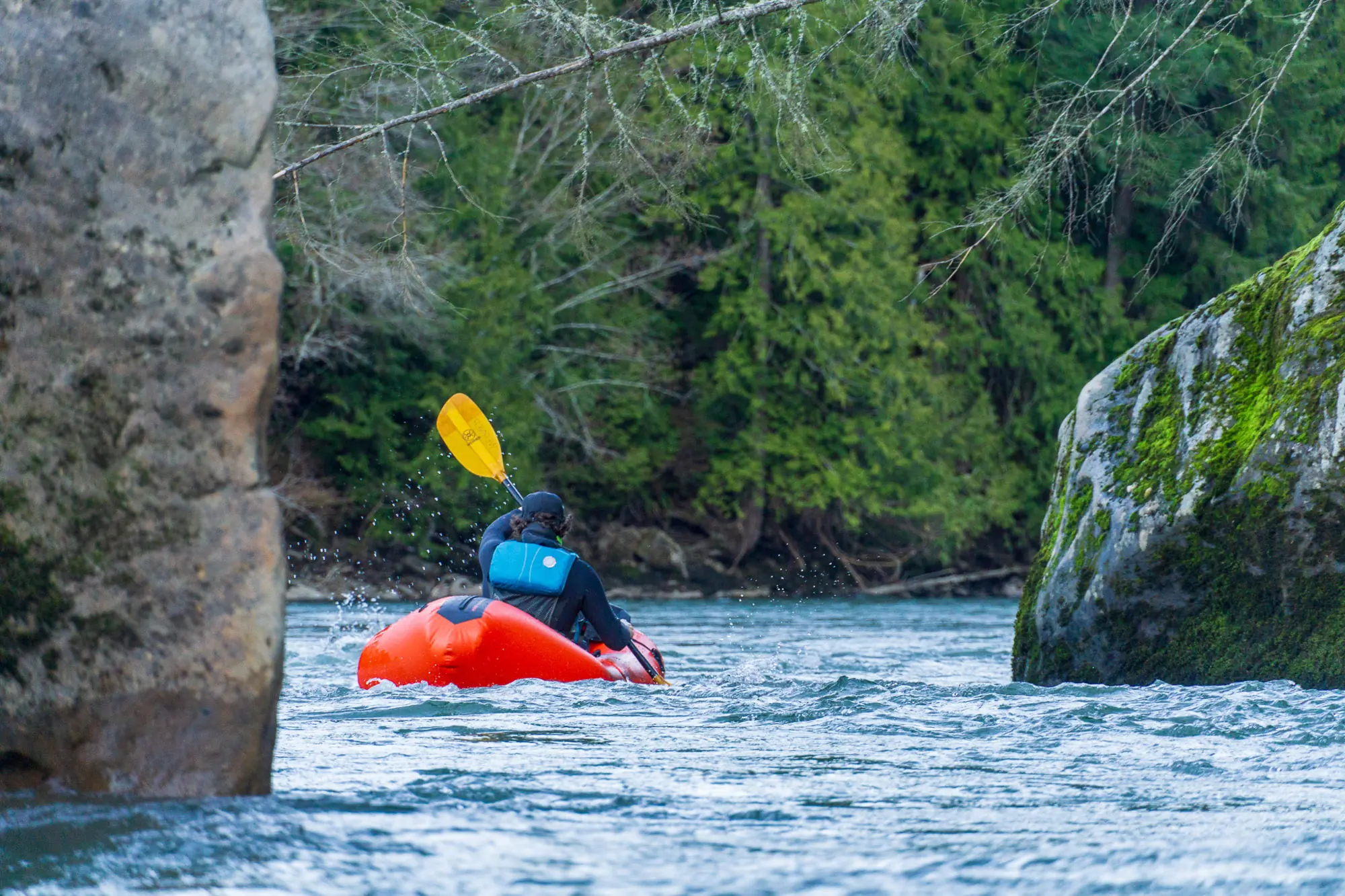 A packrafter passes between two boulders on the Nooksack River in Washington State