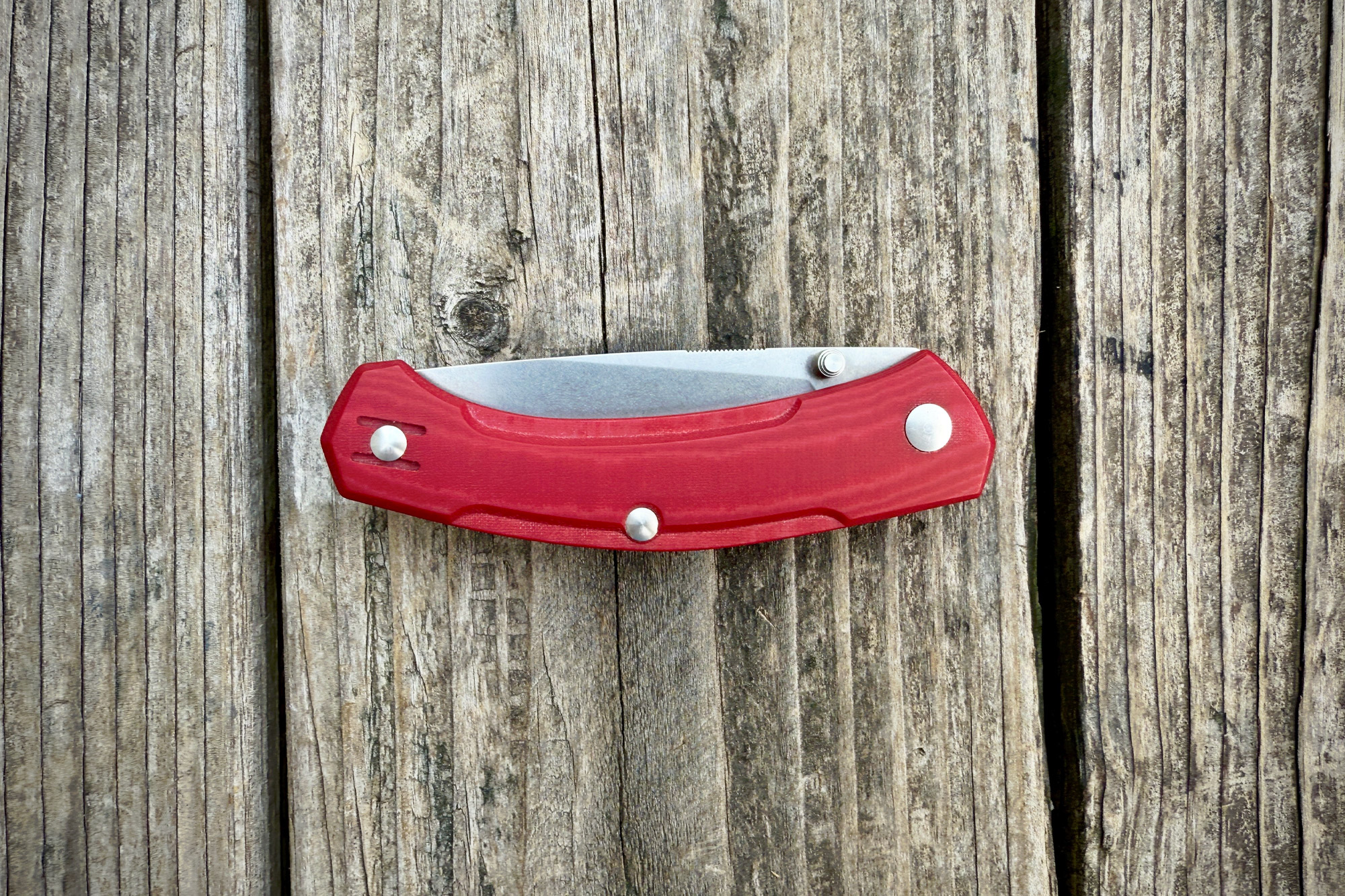 Top-down view of the folded GiantMouse Iona V2 knife, with the red handle and steel blade visible on a weathered wooden surface