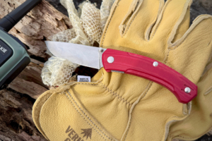 GiantMouse Iona V2 knife resting on yellow leather gloves with a green radio and honeycomb packaging in the background