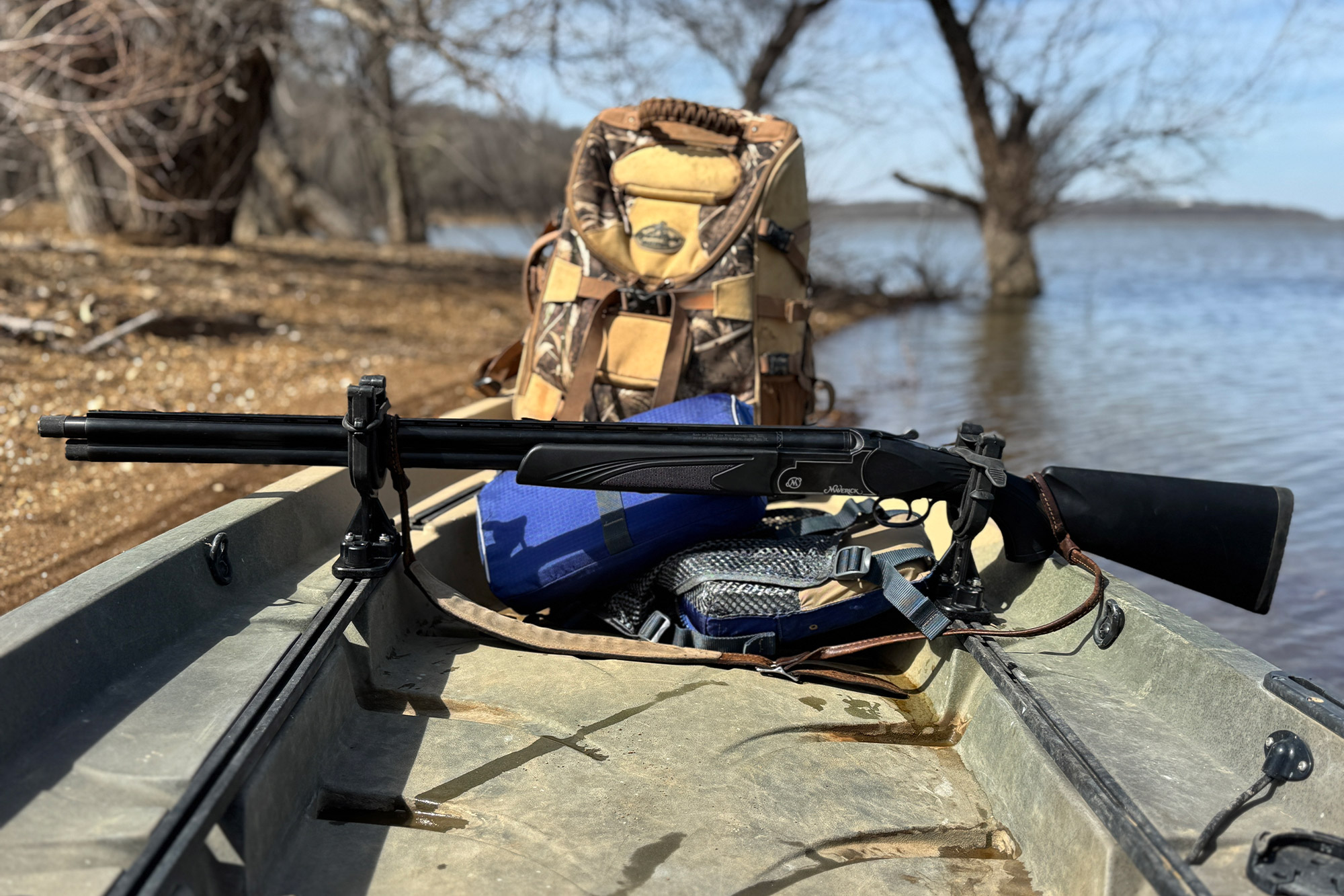 A hunting gun rests on the kayak alongside a camo backpack