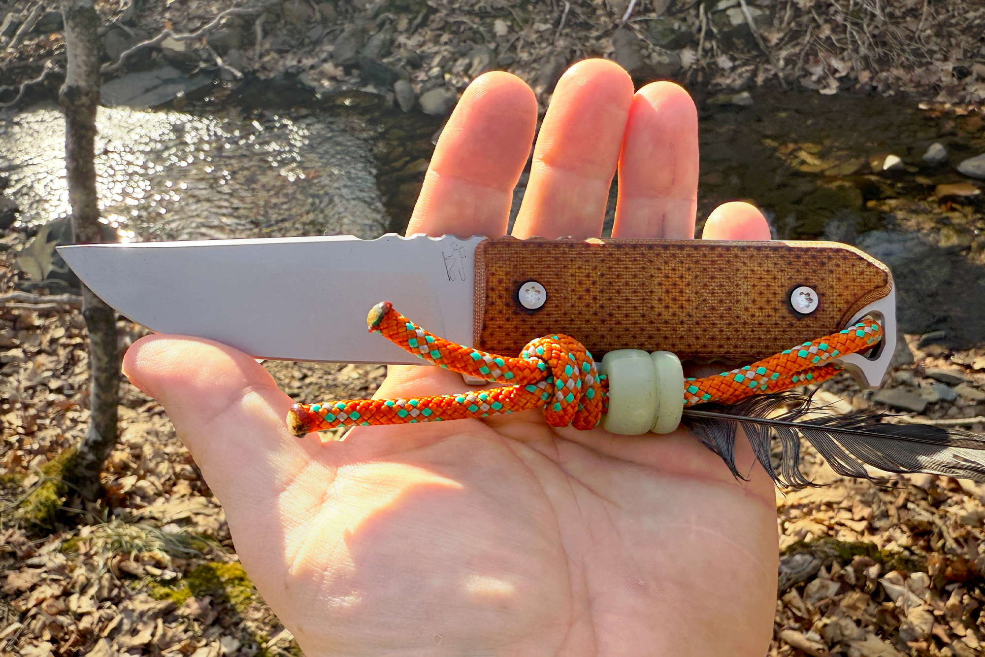 Dauntless Manufacturing Hiker with orange paracord, held in hand beside a stream