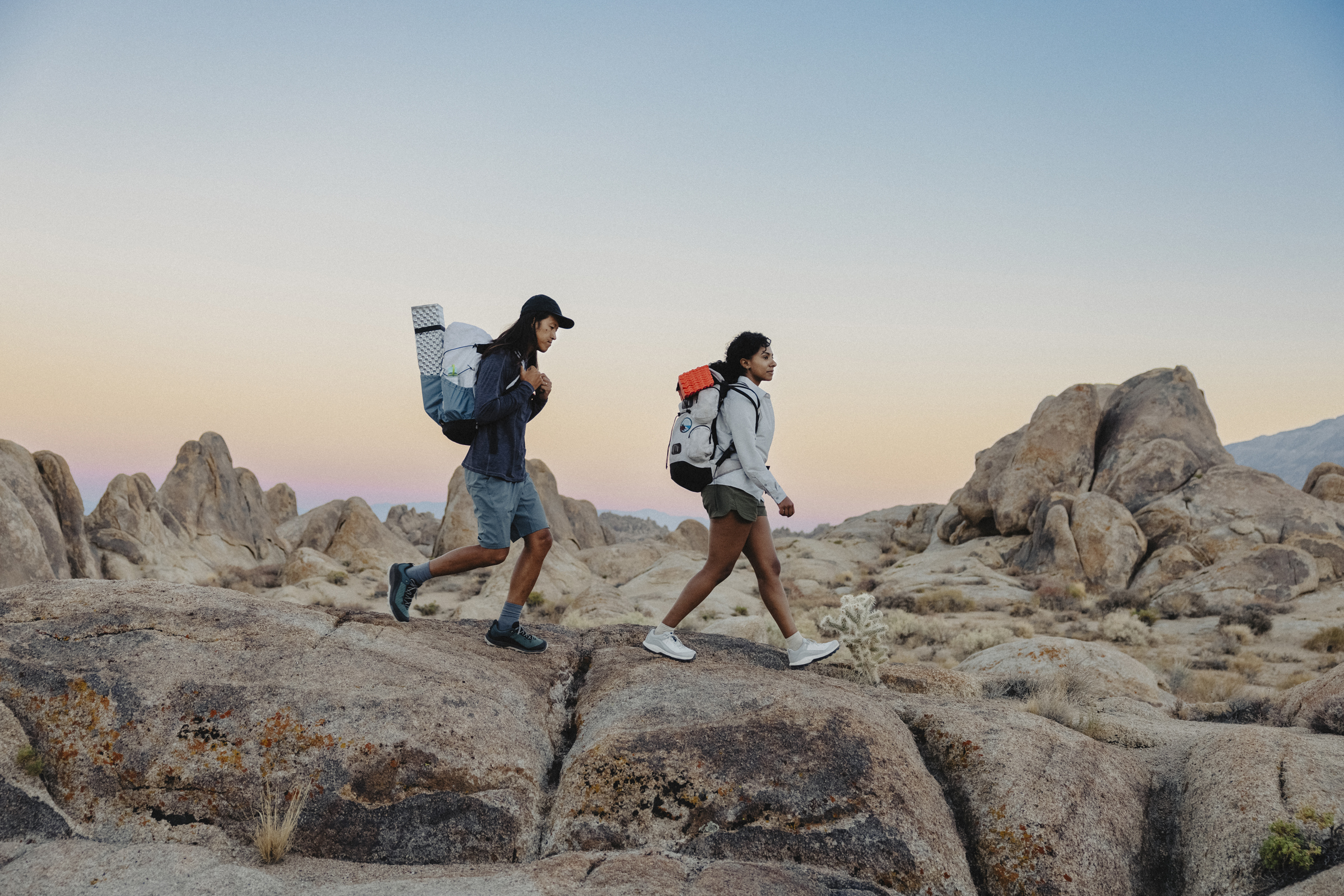 Two people hiking across rocks with cactus