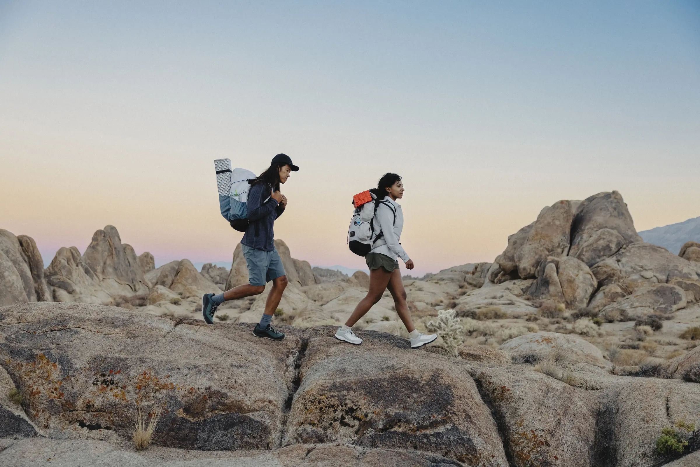 Two people hiking across rocks with cactus