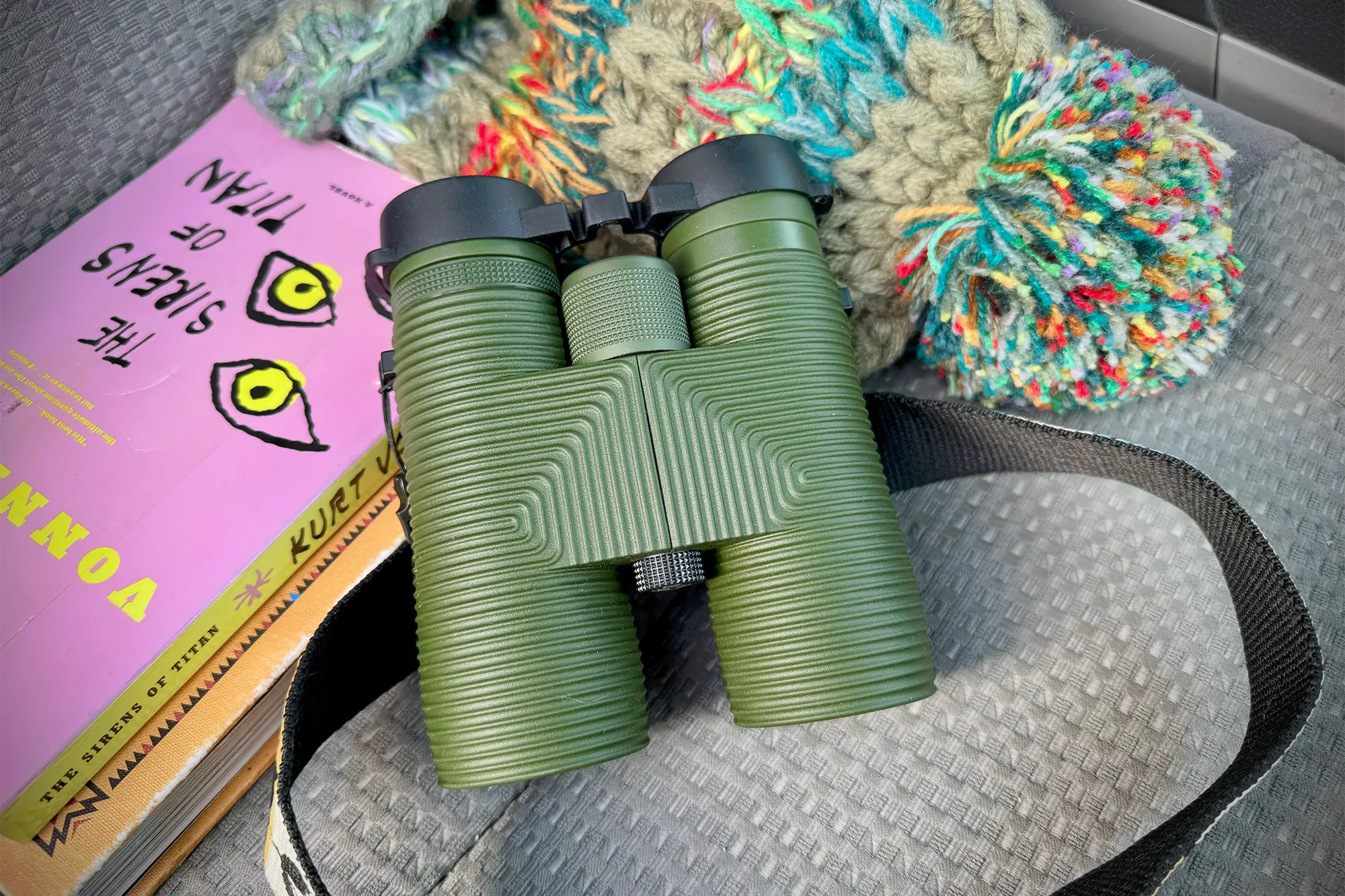 Nocs Pro Issue 8x42 resting on a car seat with books and winter gear