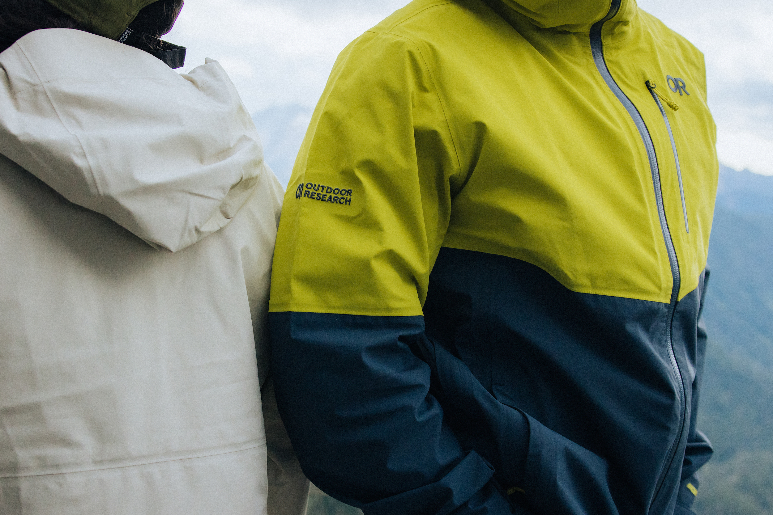 Two people in mountains wearing rain jackets.