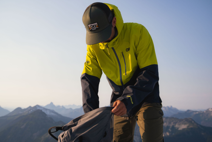 Man wearing rain jacket in mountains digs in backpack.