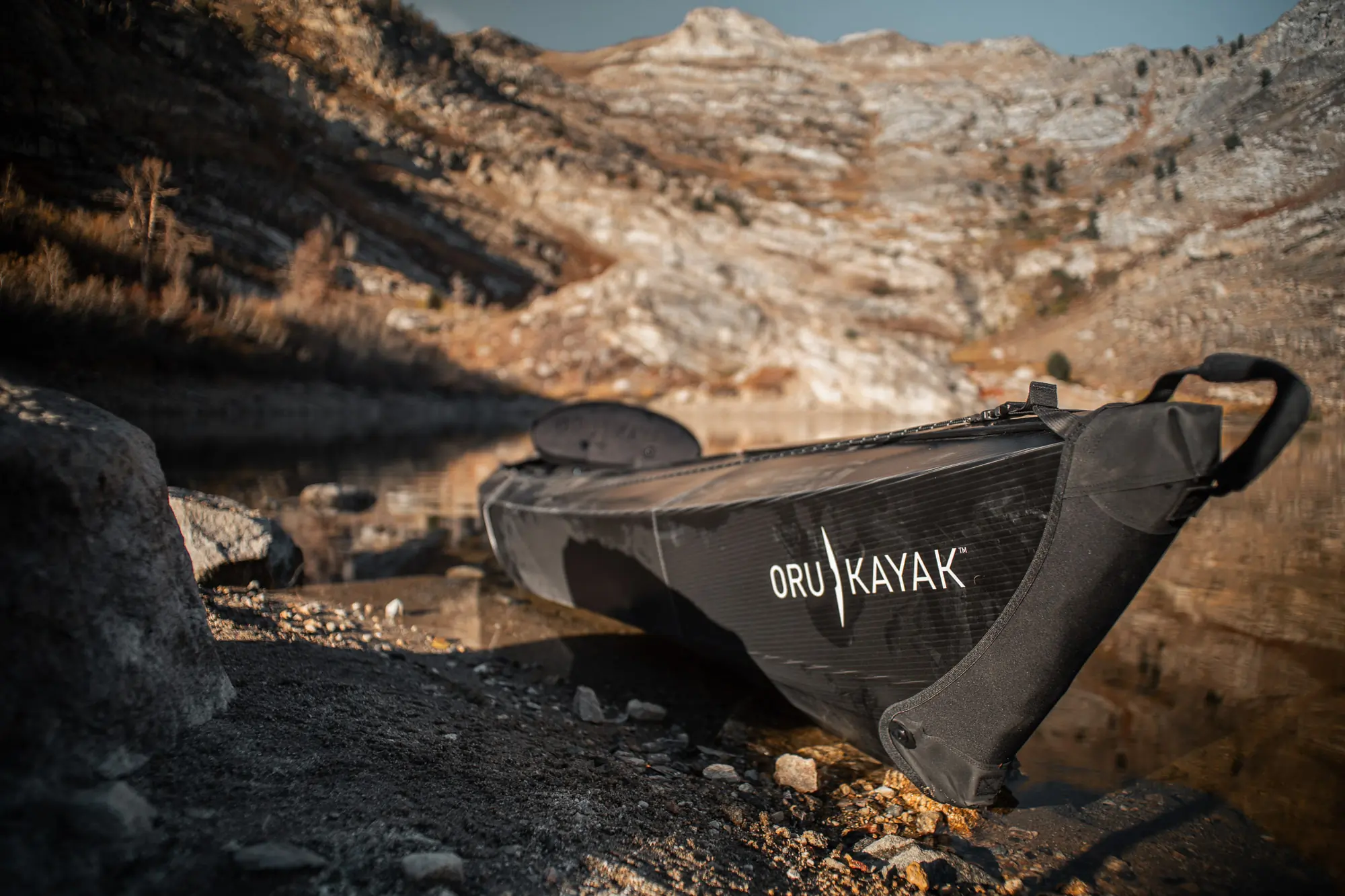 The bow of the Oru Beach LT Sport lies on shore of a lake