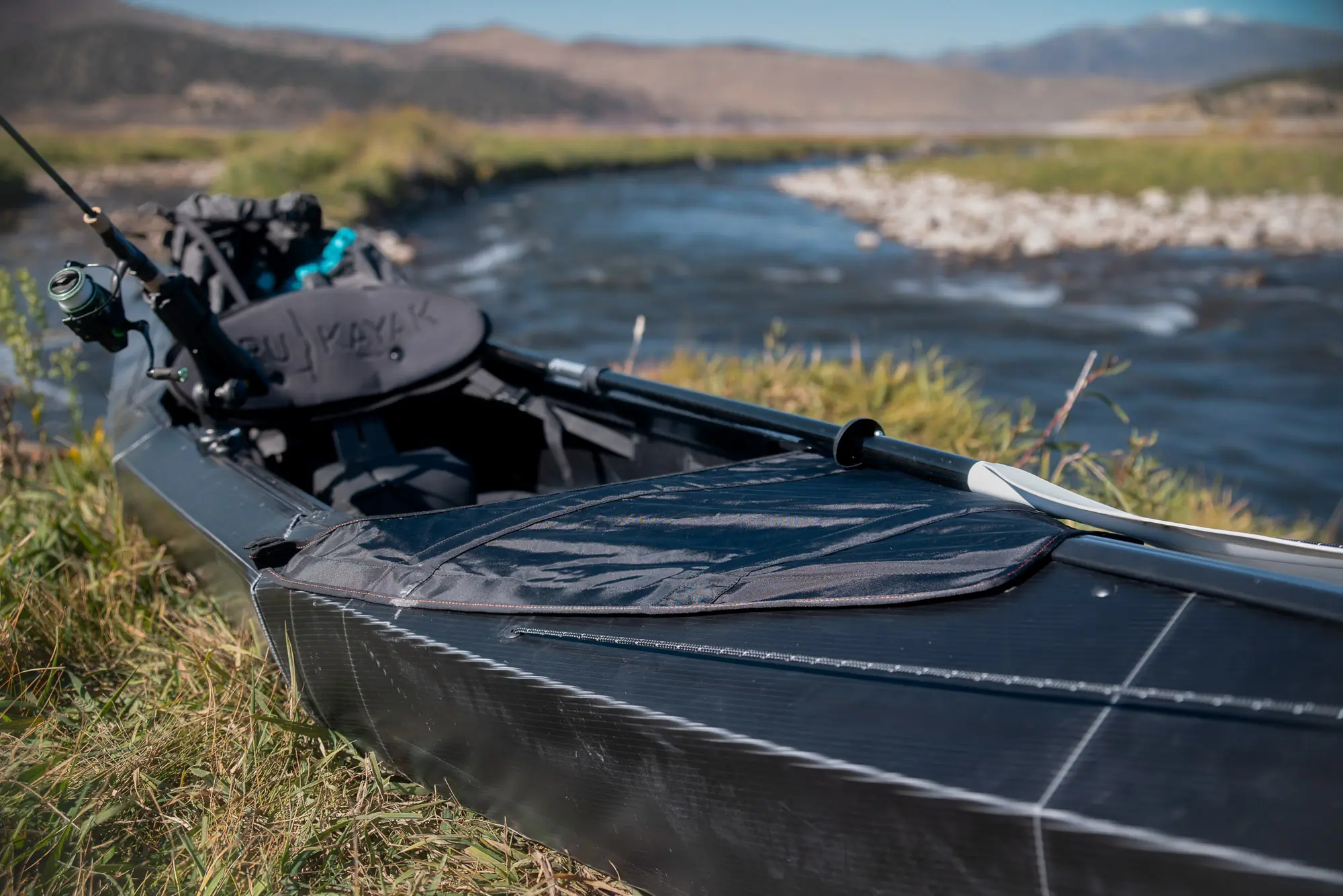 The Oru Beach Lt Sport kayak set on a river side, rigged up for paddling and fishing