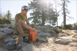 Man using orange bear canister on rocks beneath trees