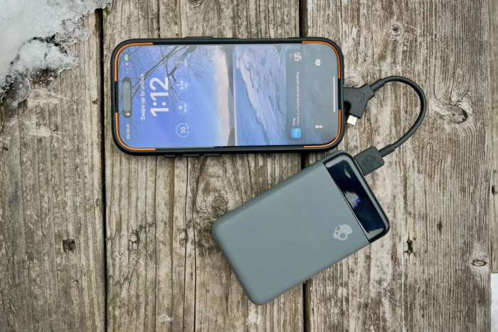 A Skullcandy Fat Stash 2 power bank is charging a phone on a wooden surface