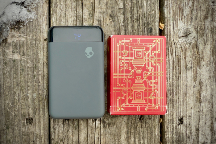 The Skullcandy Fat Stash 2 power bank is beside a red deck of cards on a wooden surface