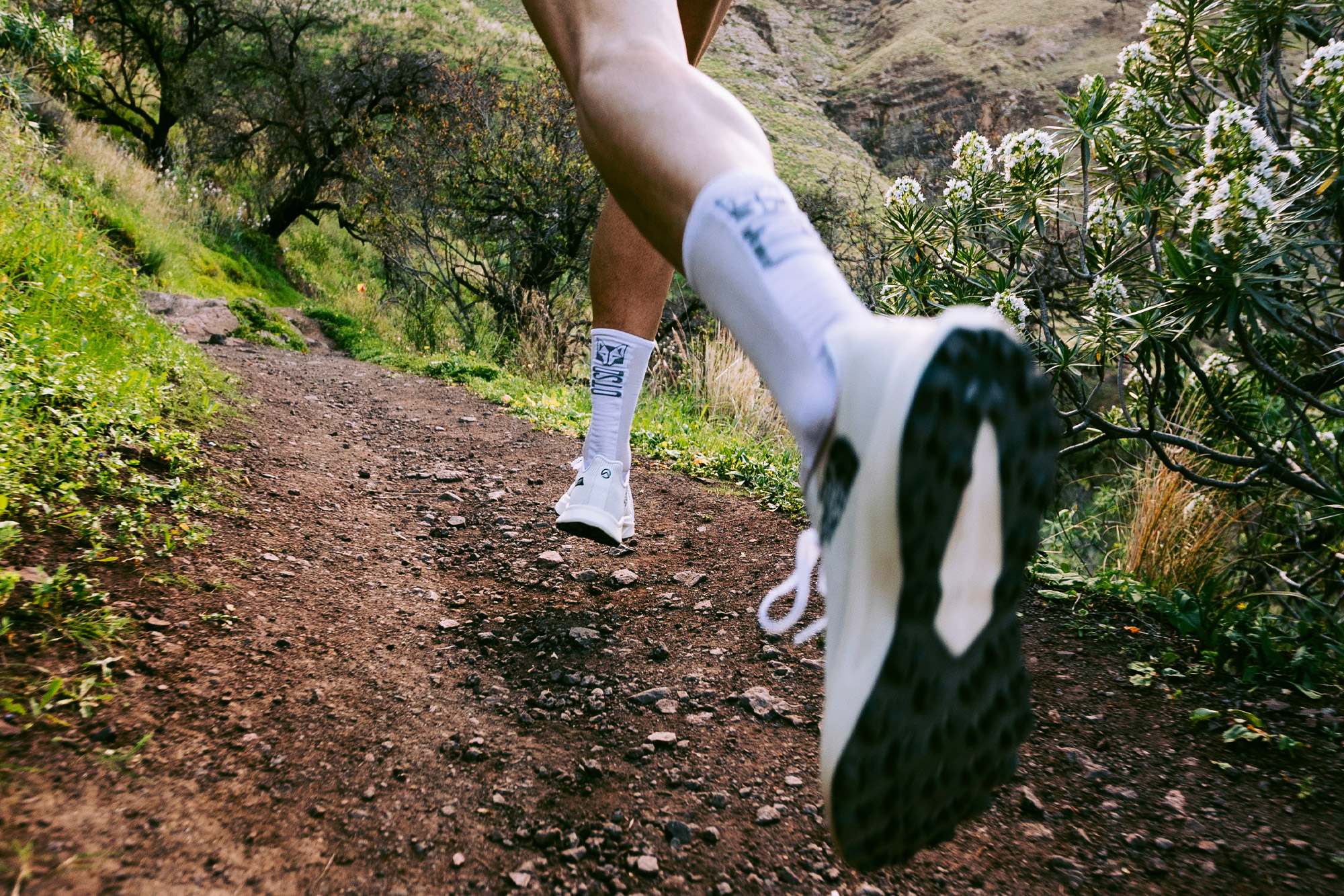 Close-up of a runner’s foot mid-stride on a dirt trail, showing the aggressive tread of the shoe