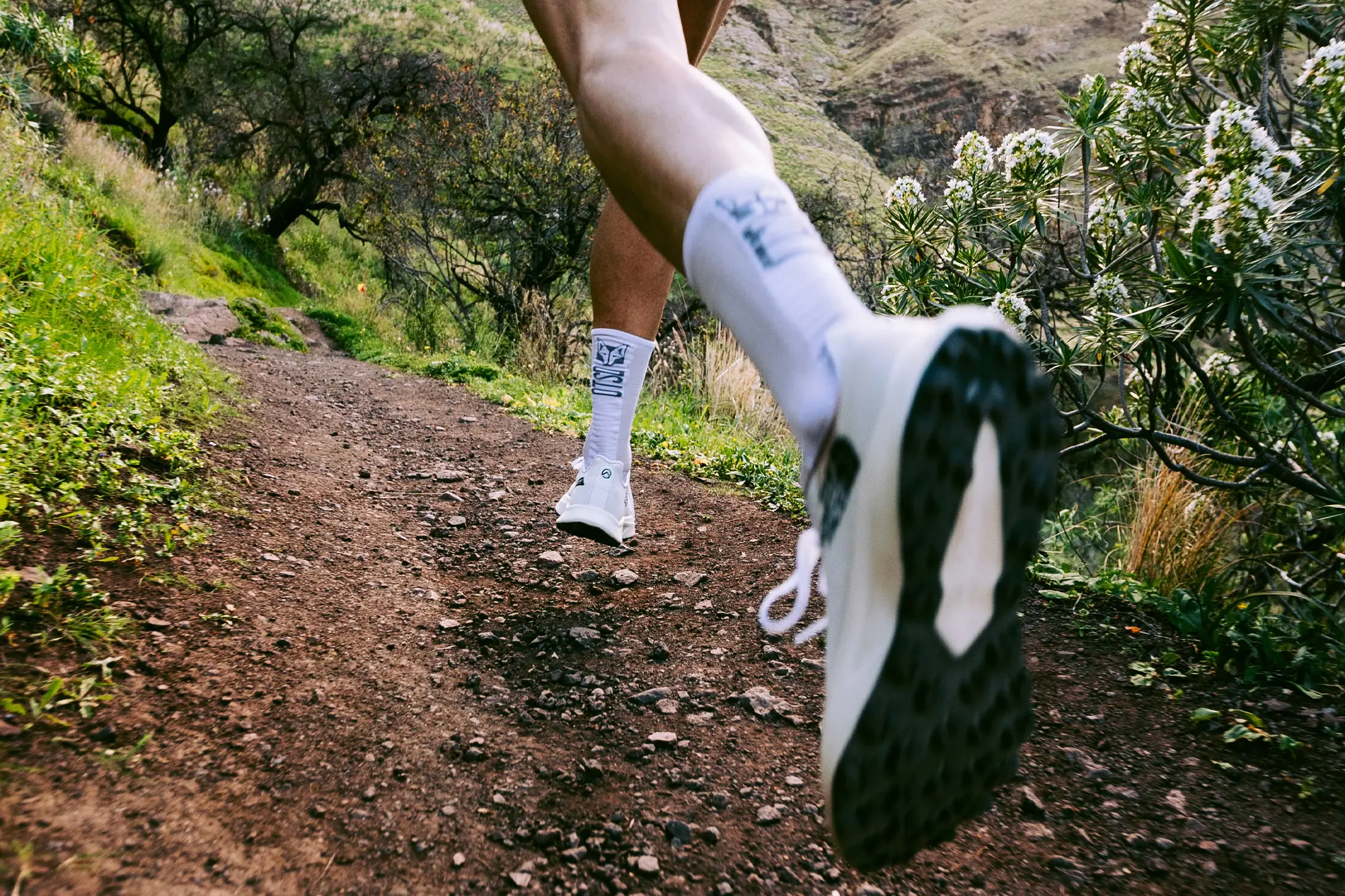 Close-up of a runner’s foot mid-stride on a dirt trail, showing the aggressive tread of the shoe