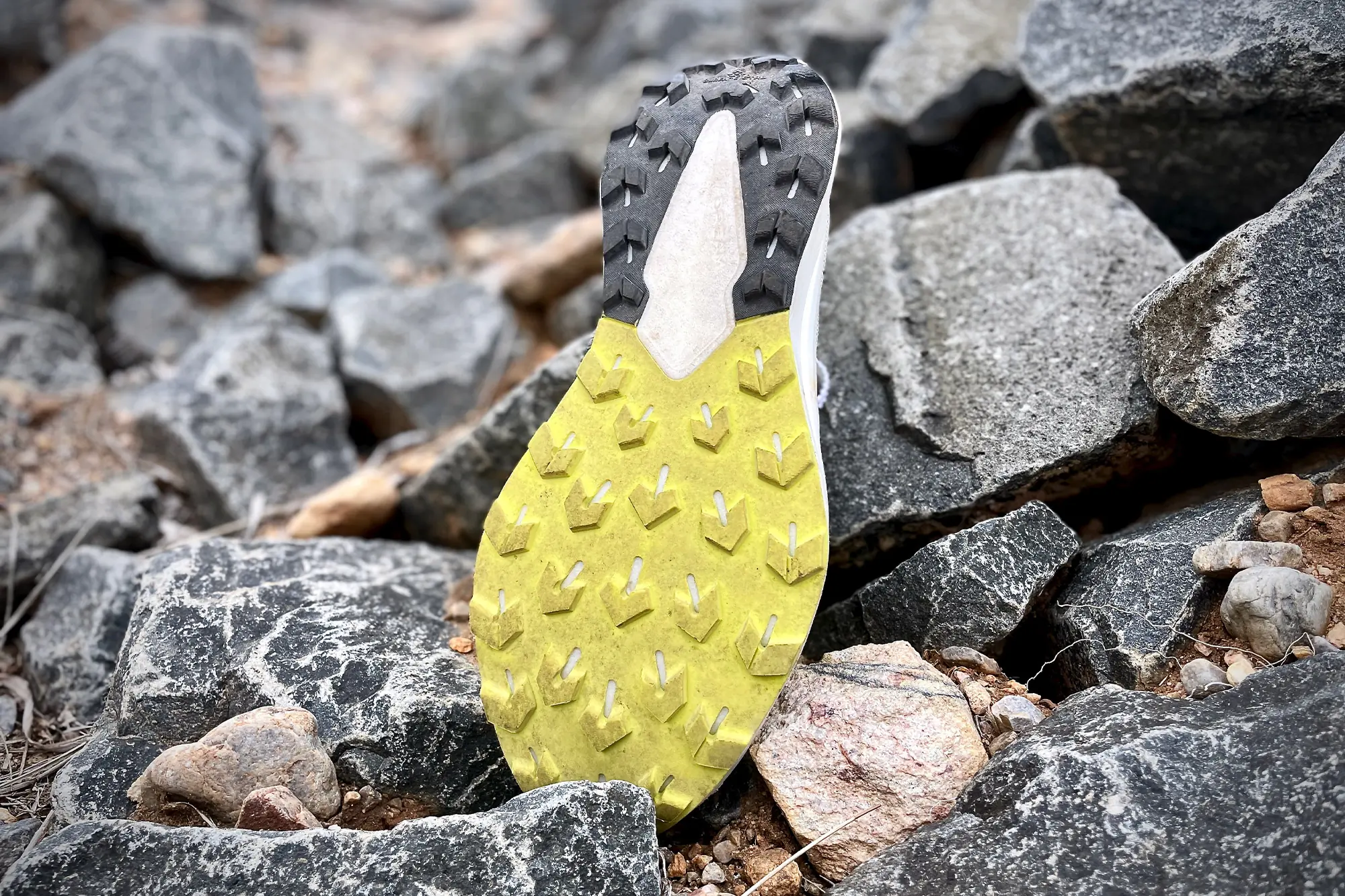 A close-up of a yellow and black trail running shoe sole on rocky ground