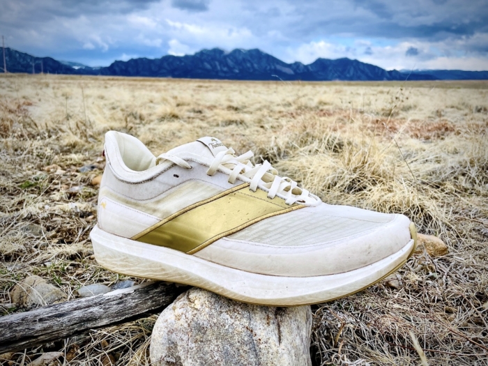 The Tracksmith Eliot Racer placed on a rock with a mountain backdrop under a cloudy sky