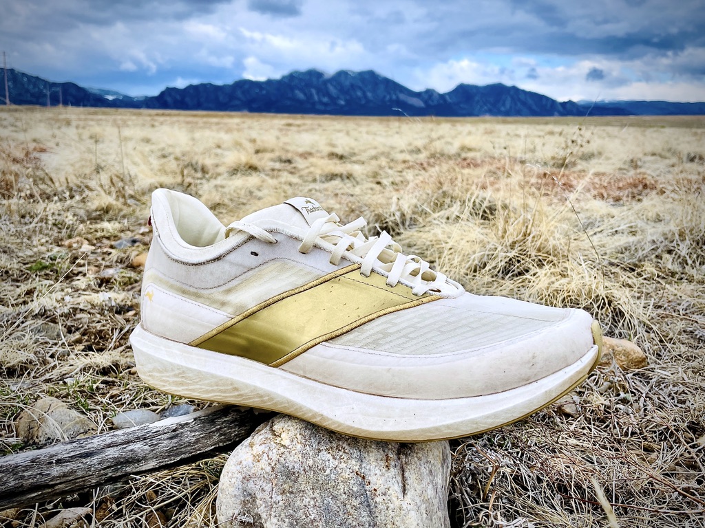 The Tracksmith Eliot Racer placed on a rock with a mountain backdrop under a cloudy sky