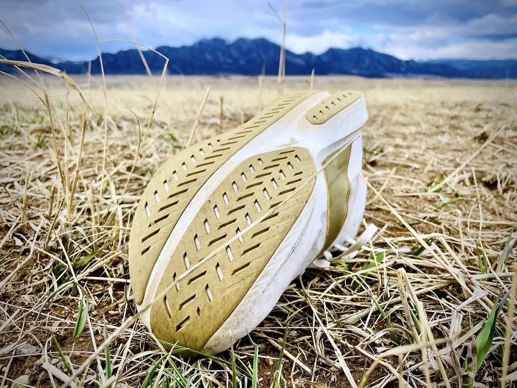 The textured sole of the Tracksmith Eliot Racer rests on dry grass with mountains in the background