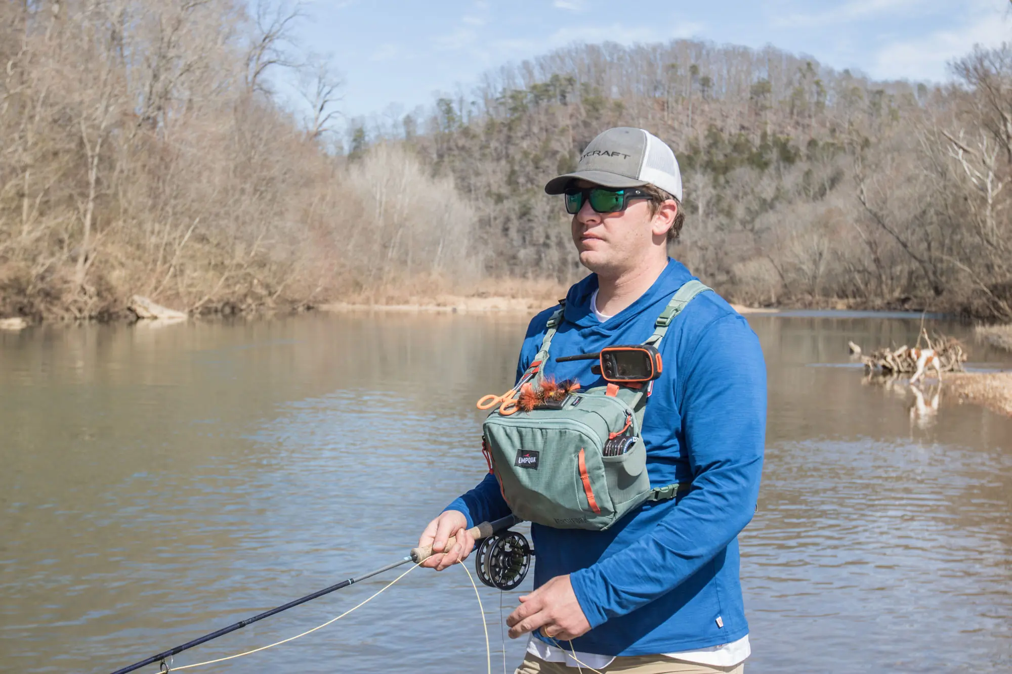 An angler wears the Umpqua Northfork Chest Pack while fishing. A dog jumps in the river in the background