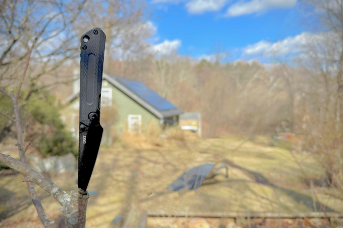 CRKT Straight embedded in a tree branch, with a solar-powered home in the background