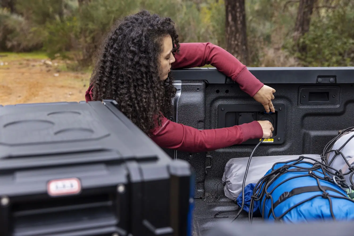 A woman plugs a cable into the power outlet in a Ford Ranger's truck bed