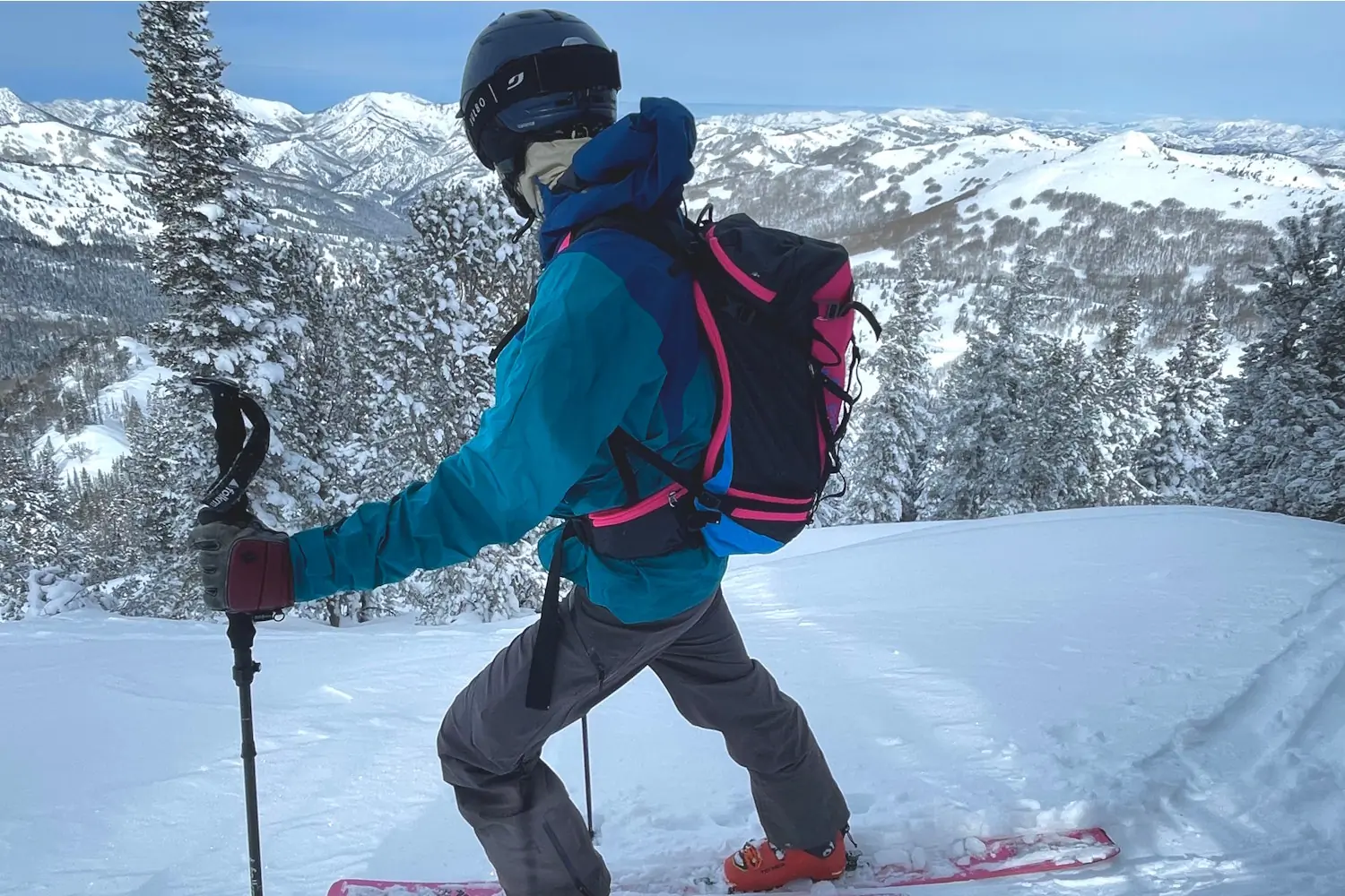 Skier in blue jacket and black helmet ascending a snowy slope with a Pingora Vivid 27L backpack