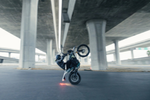 A rider performing a wheelie on the Zero FX electric motorcycle under an overpass