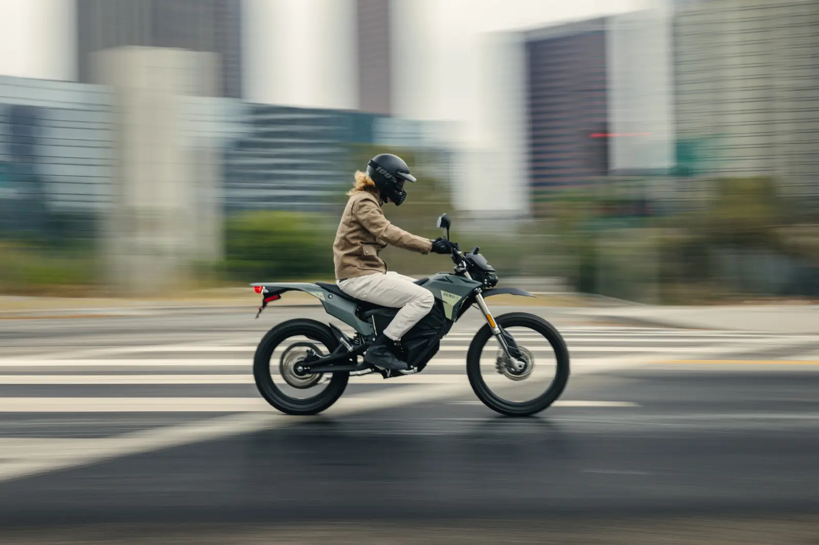 A rider on the Zero FX electric motorcycle in motion on an urban street with tall buildings in the background