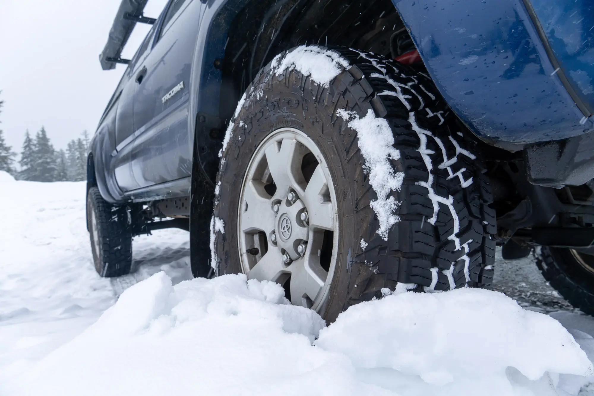 A blue truck drives through deeper snow and shows off the tread pattern